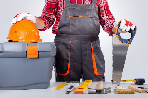 Handwerker in einheitlicher stehender Haltesäge auf Holz und Werkzeugkasten mit Instrument auf der Werkbank.