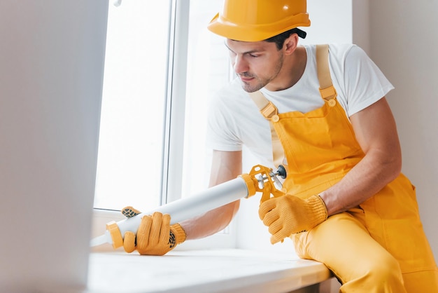 Handwerker in gelber Uniform arbeitet mit Kleber für Fenster im Innenbereich Hausrenovierung Konzeption