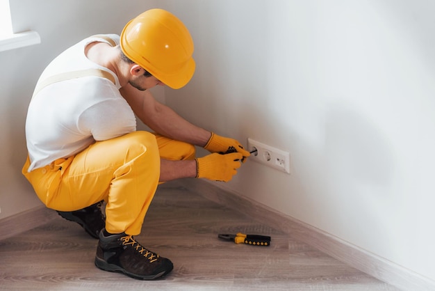 Handwerker in gelber Uniform arbeitet mit Strom und installiert neue Steckdose Hausrenovierungskonzeption