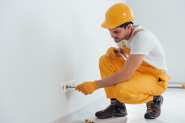 Handwerker in gelber Uniform arbeitet mit Strom und installiert neue Steckdose Hausrenovierungskonzeption