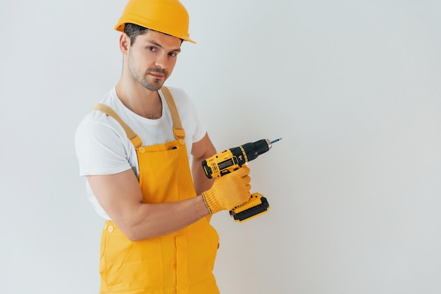 Handwerker in gelber Uniform, der mit automatischem Schraubendreher an der weißen Wand steht Konzept für die Renovierung des Hauses