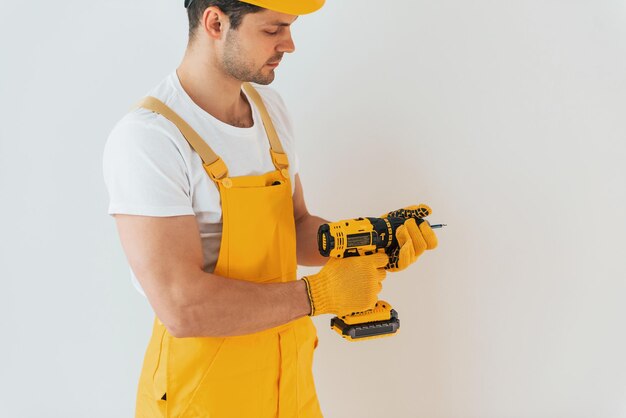 Handwerker in gelber Uniform, der mit automatischem Schraubendreher an der weißen Wand steht Konzept für die Renovierung des Hauses