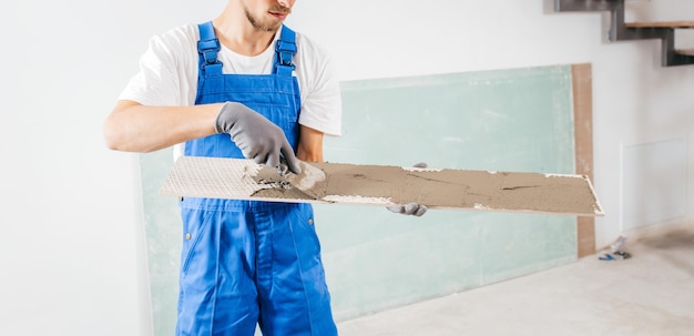 Handwerker in grauen Handschuhen und spezieller Uniform, die in einem neuen Haus Zement auf Fliesen legt