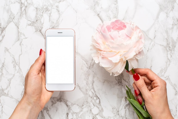 Handy in der Hand mit weiße und rosa piony Blumen auf einer Marmoroberfläche