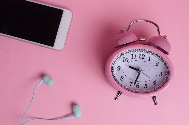 Handy-Kopfhörer und Wecker auf rosa Hintergrund