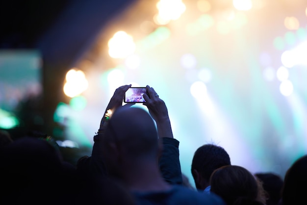 Handy-Mobiltelefon und -fotografie bei einem Musikkonzert in der Menge für Social-Media-Post für Feiertage, Karneval oder Nacht Silhouette-Foto und Sommerveranstaltung oder Reiseparty oder dunkle Außenbeleuchtung oder Festival
