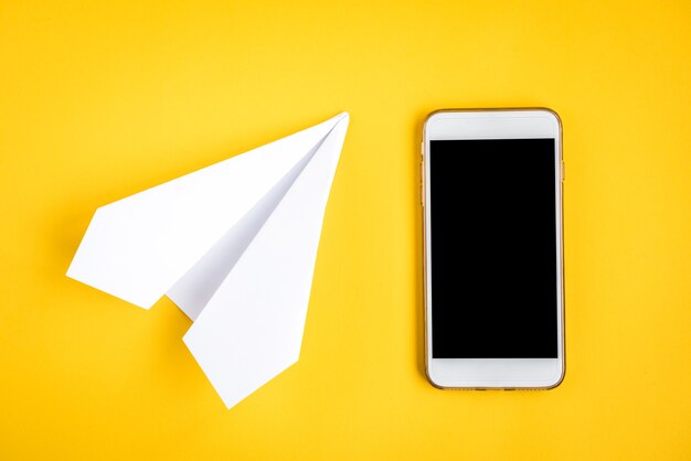 Handy und Papierflugzeug auf gelb