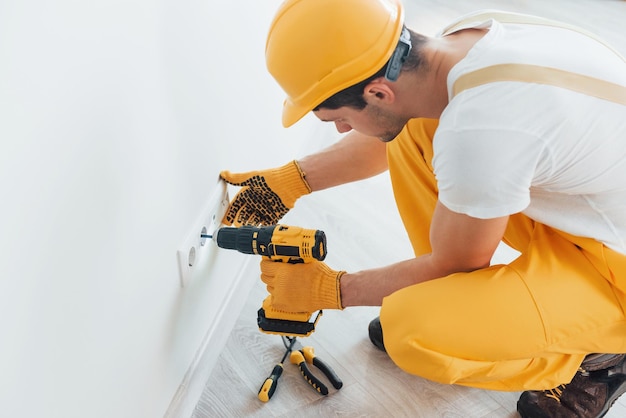 Handyman em uniforme amarelo trabalha com eletricidade e instalando novo soquete usando chave de fenda automática Concepção de renovação de casa