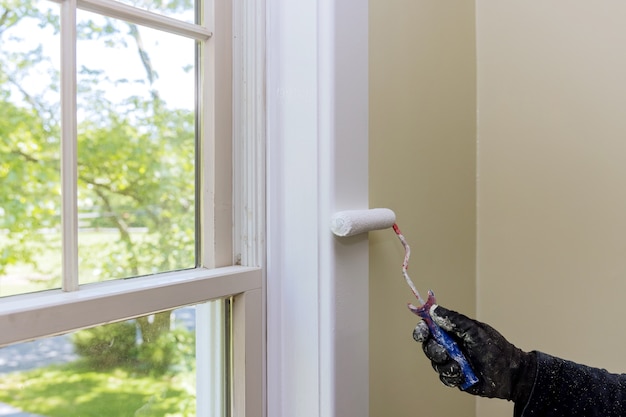 Handyman pinta uma moldura de janela com um rolo de pintura na reforma de casa