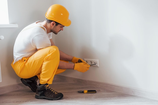 Handyman en uniforme amarillo trabaja con electricidad e instalando un nuevo zócalo Concepción de renovación de la casa