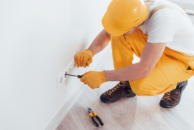 Handyman en uniforme amarillo trabaja con electricidad e instalando un nuevo zócalo Concepción de renovación de la casa