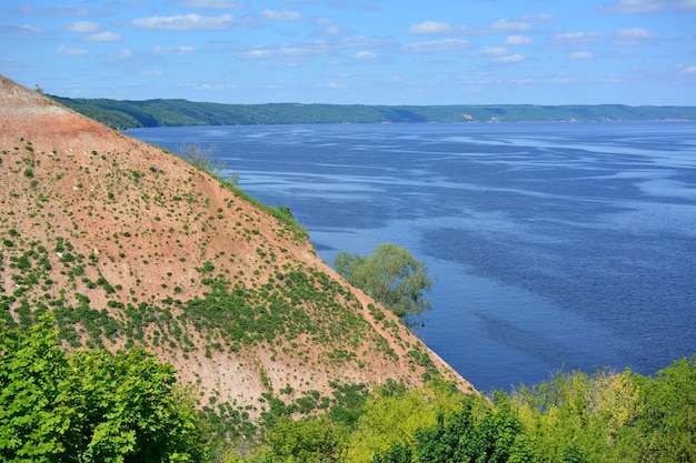 Hang des Berges mit rotem Schlamm und grünen Büschen und blauem Fluss im Hintergrund