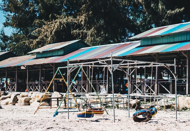 Hang Seil Schaukel alte Reifen malen leuchtend mehrfarbig orange blau gelb rot Metallrahmen Veranda Dach Natur Sandstrand Hintergrund Tag Sonne Sommer Kind Kindergarten Reise Freude Sandkasten Spielplatz