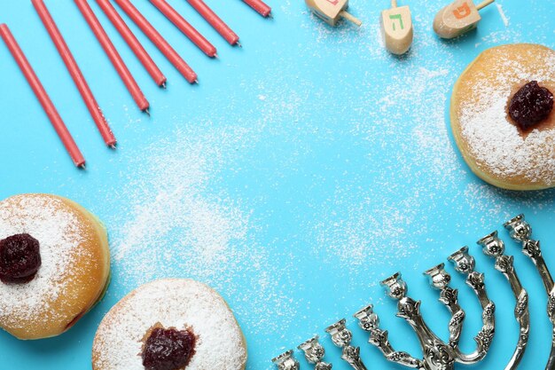 Hanukkah tradicional menorah velas donuts dreidels con letras He Pe Nun Gimel sobre fondo azul claro espacio plano para texto