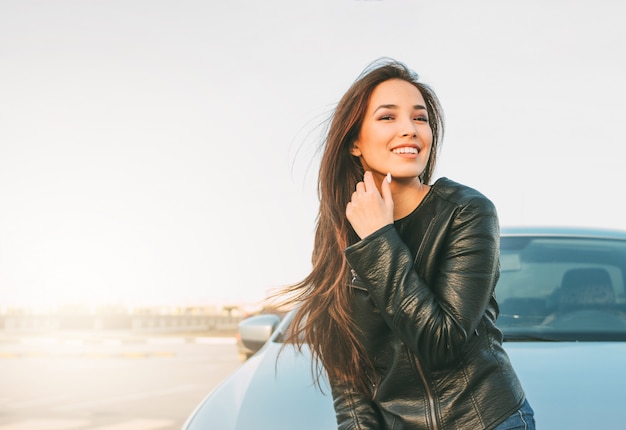 Foto happpy hermosa encantadora morena de pelo largo joven asiática en chaqueta de cuero negro cerca de su coche