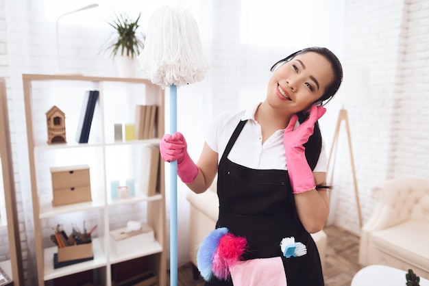 Happy asian maid with mop está escuchando música