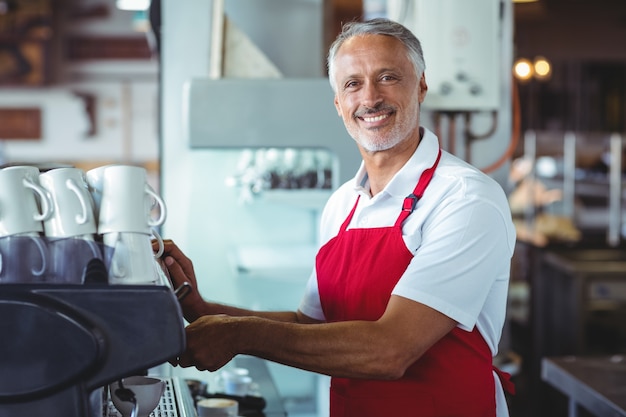 Happy barista sorrindo para a câmera e usando a máquina de café