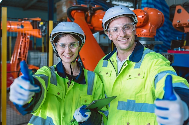 Happy Engineer Team Portrait Daumen hoch genießen die Zusammenarbeit in einer modernen Metallfabrik mit Roboterarm