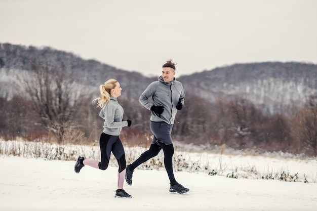 Happy Fit sportliches Paar, das in der Natur am verschneiten Wintertag läuft. Fitness im Freien, gesundes Leben, Winterfitness