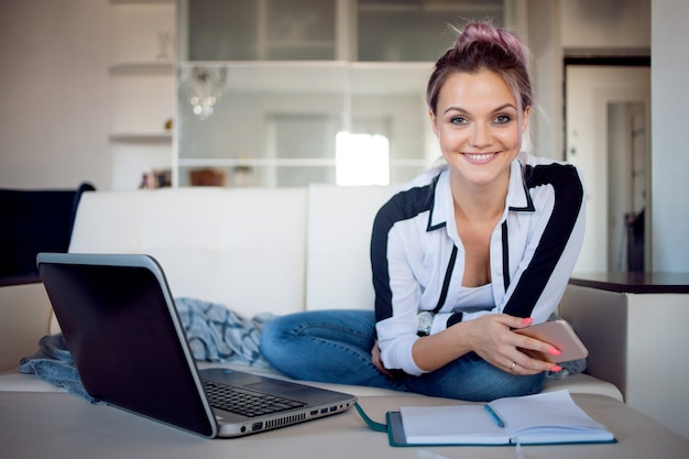 Happy freelance trabaja en casa. Mujer joven con la computadora portátil en el sofá.