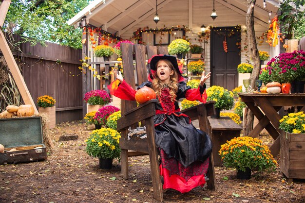 Happy Halloween ein Mädchen in einem Hexenkostüm mit einem Kürbis, der sich im Herbst in der Nähe des Hauses amüsiert