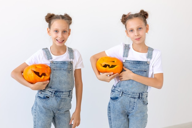 Happy Halloween, Feiertage und Kindheitskonzept - Niedliche kleine Zwillingsschwesternmädchen mit einer Kürbis-Kürbislaterne, die Spaß haben, während sie Zeit drinnen verbringen.