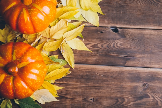 Happy Halloween-Konzept mit orangefarbenen Kürbissen und gelben Blättern auf Holzuntergrund