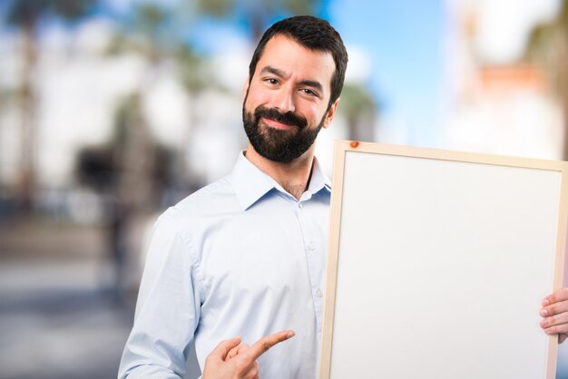 Happy Handsome Mann mit Bart mit einem leeren Plakat auf unfocused Hintergrund