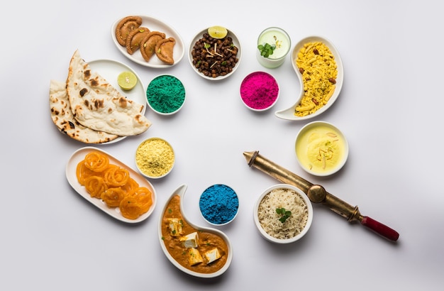 Foto happy holy konzept zeigt indisches mittagessen wie paneer butter masala naan jeera reis black chana fry jalebi ras malai thandai und farsan mit holi-farben und pichkari