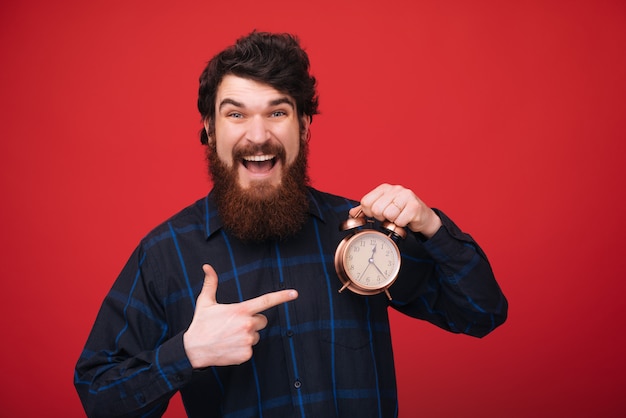 Happy hours. Habilidades de gestão de tempo. Homem barbudo cara madura segurar relógio isolado sobre parede vermelha