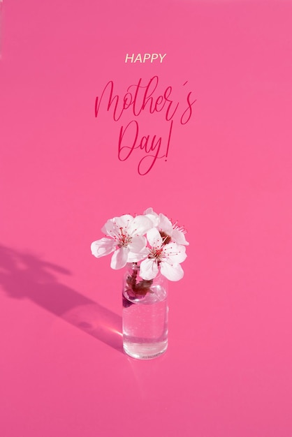 Happy Mothers Day Grußkarte mit Miniatur-Glasflasche mit Blumen auf rosa Hintergrund. Hochformat.
