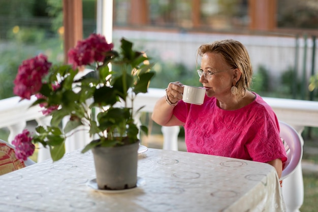 Happy Senior Frau sitzt auf der Veranda mit Kaffeetasse Gepflegte Rentnerin sitzt und lächelt auf der Terrasse mit einer Tasse Tee Ruhestandskonzept