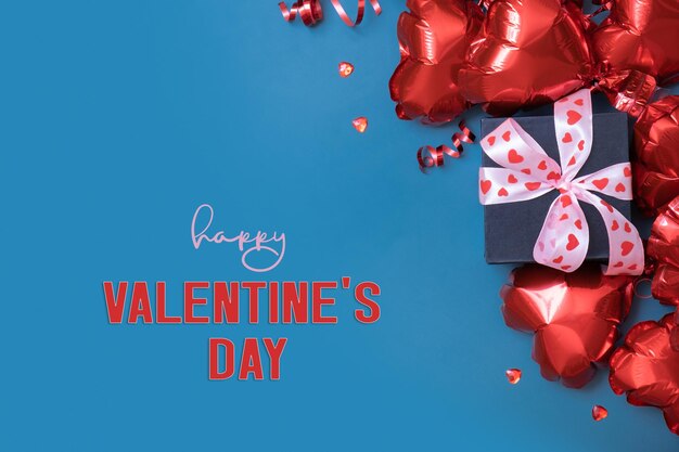 Happy Valentines Day Text mit Geschenkbox und roten Luftballons in Herzform auf blauem Hintergrund Valentinstag-Grußkarte