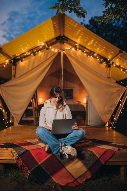 Happy Woman Freelancer mit einem Laptop auf einem gemütlichen Glamping-Zelt an einem Sommerabend Luxus-Campingzelt für Outdoor-Urlaub und Urlaub Lifestyle-Konzept