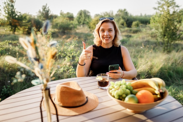 Happy Woman Freelancer nutzen Telefon und trinken Cocktailanrufe, während sie sich an sonnigen Tagen in einem gemütlichen Glamping-Zelt entspannen Luxus-Campingzelt für Sommerferien und Urlaub im Freien Lifestyle-Konzept