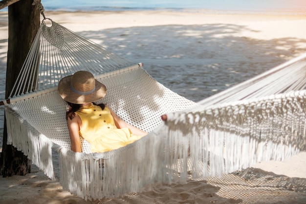 Happy Woman Traveler se relaja en una hamaca en la playa del paraíso Mujer turista en vestido amarillo descansa cerca del mar tropical vacaciones viajes verano Wanderlust y concepto de vacaciones