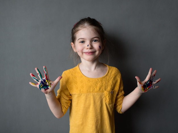 Happycute kleines Mädchen mit farbigen Händen auf einem grauen Hintergrund junger Künstler