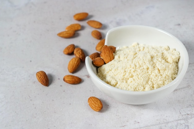 Harina de almendras en un bol y una cuchara con nueces esparcidas sobre un fondo de hormigón blanco