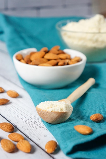 Harina de almendras frescas en una cuchara de madera con almendras en un espacio de copia de mesa de madera blanca