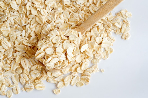 Harina de avena en una cuchara de madera sobre un fondo blanco. Concepto de comida sana, vista superior.