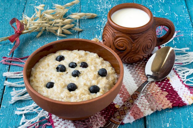 Harina de avena en un cuenco de arcilla taza de leche estera casera tallos de avena sobre un fondo de madera azul