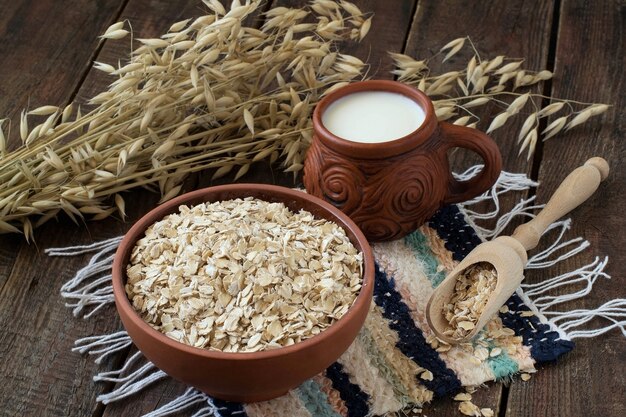 Harina de avena en un cuenco de barro y una cuchara de madera taza de leche tallos de avena