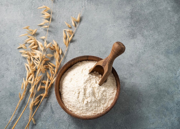 Harina de avena en un cuenco de madera con una cuchara sobre un fondo azul con ramas de avena seca Producto orgánico y saludable para hornear en casa