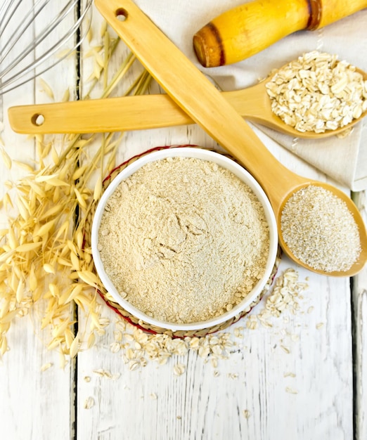 Harina de avena en un tazón blanco, avena y salvado en una cuchara de madera, tallos de avena en el fondo de las tablas de madera en la parte superior