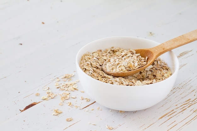 Harina de avena en un tazón blanco, fondo de madera