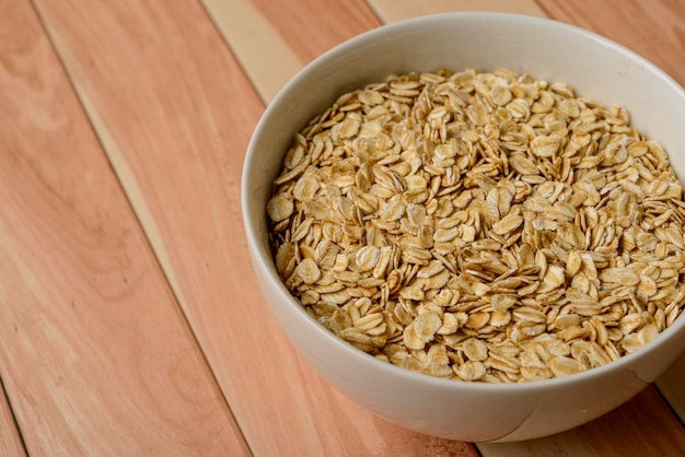 Harina de avena en tazón de fuente blanco sobre mesa de madera