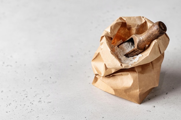 Harina en bolsa de papel artesanal marrón con cuchara de madera sobre fondo blanco espacio de copia de estilo rústico