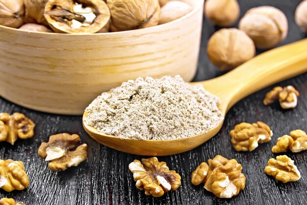 Harina de nuez en una cuchara, nueces en un tazón y sobre la mesa en el fondo de la tabla de madera oscura.