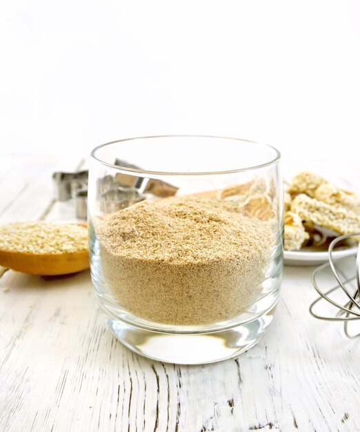 Harina de sésamo en un vaso, una cuchara con cortadores de galletas de semillas de sésamo y una galleta mezcladora en el fondo de tablas de madera