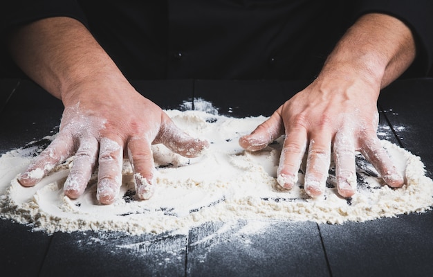 Harina de trigo blanca en una mesa de madera negra y dos manos masculinas